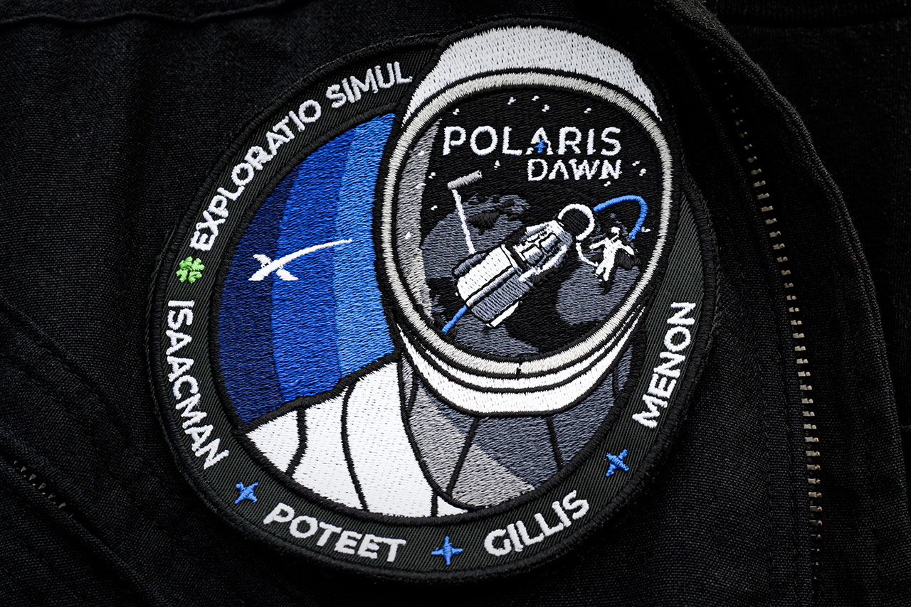 The Polaris Dawn mission patch depicts a spacewalking astronaut outside of SpaceX's Dragon spacecraft as reflected in the spacesuit visor of another crew member.
