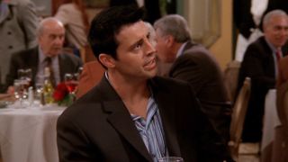 Matt LeBlanc as Joey Tribbiani looks angry as he sits at a table in a restaurant.