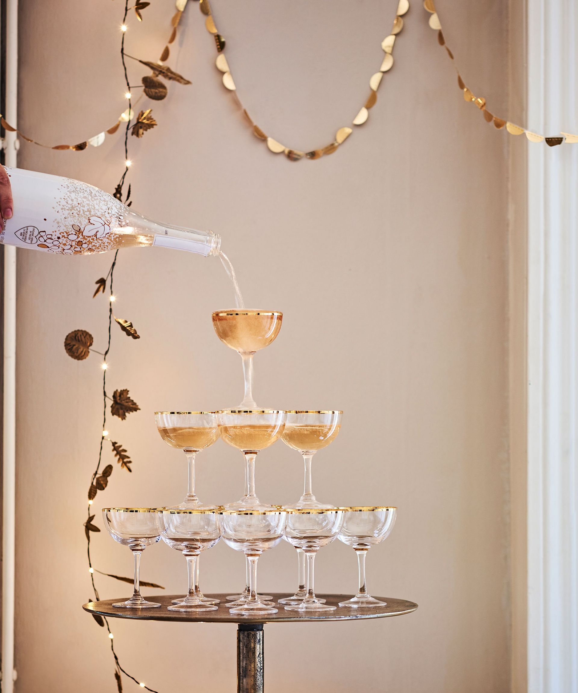 A small round table with a pyramid of wine glasses and wine being poured from a white and gold bottle.