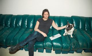 A man is sitting in green colored sofa with dog.