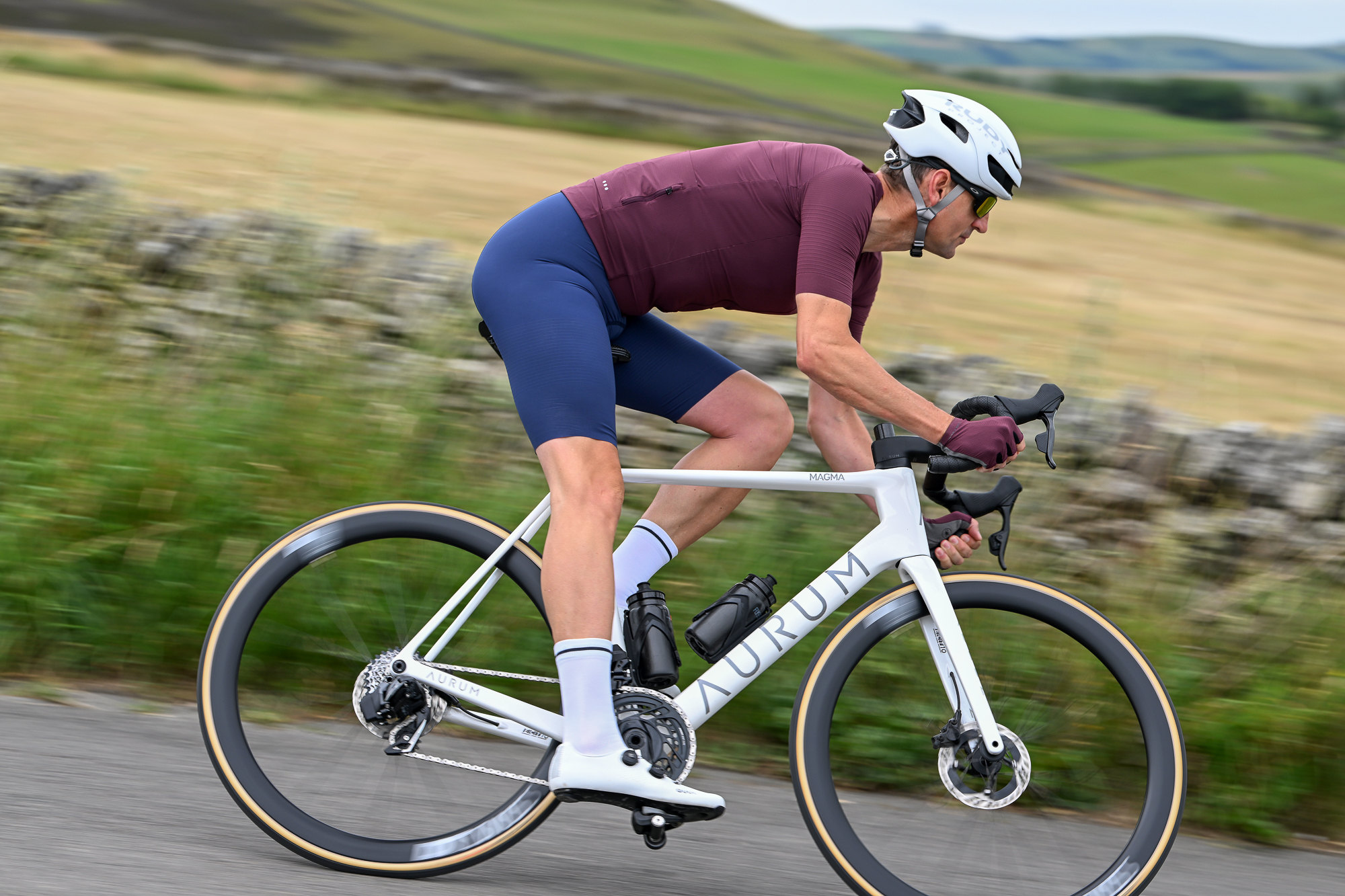 man riding a bike downhill round a corner wearing a purple jersey and white helmet