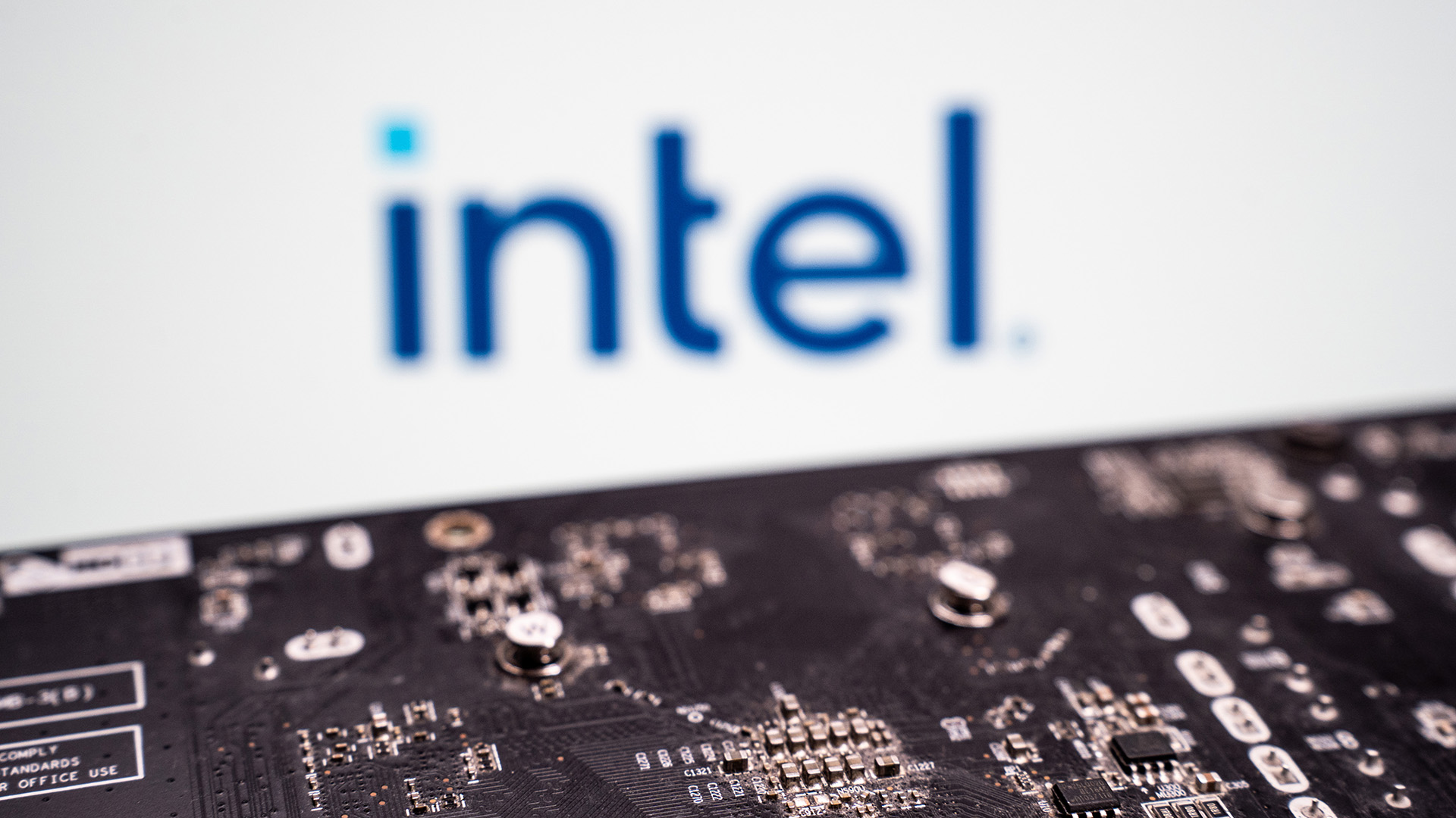 A close-up shot of a printed circuit board, with the Intel logo in blue on a white background out of focus behind.