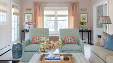 a living room with two blue printed chairs with matching pillows, a vase of flowers on the ottoman