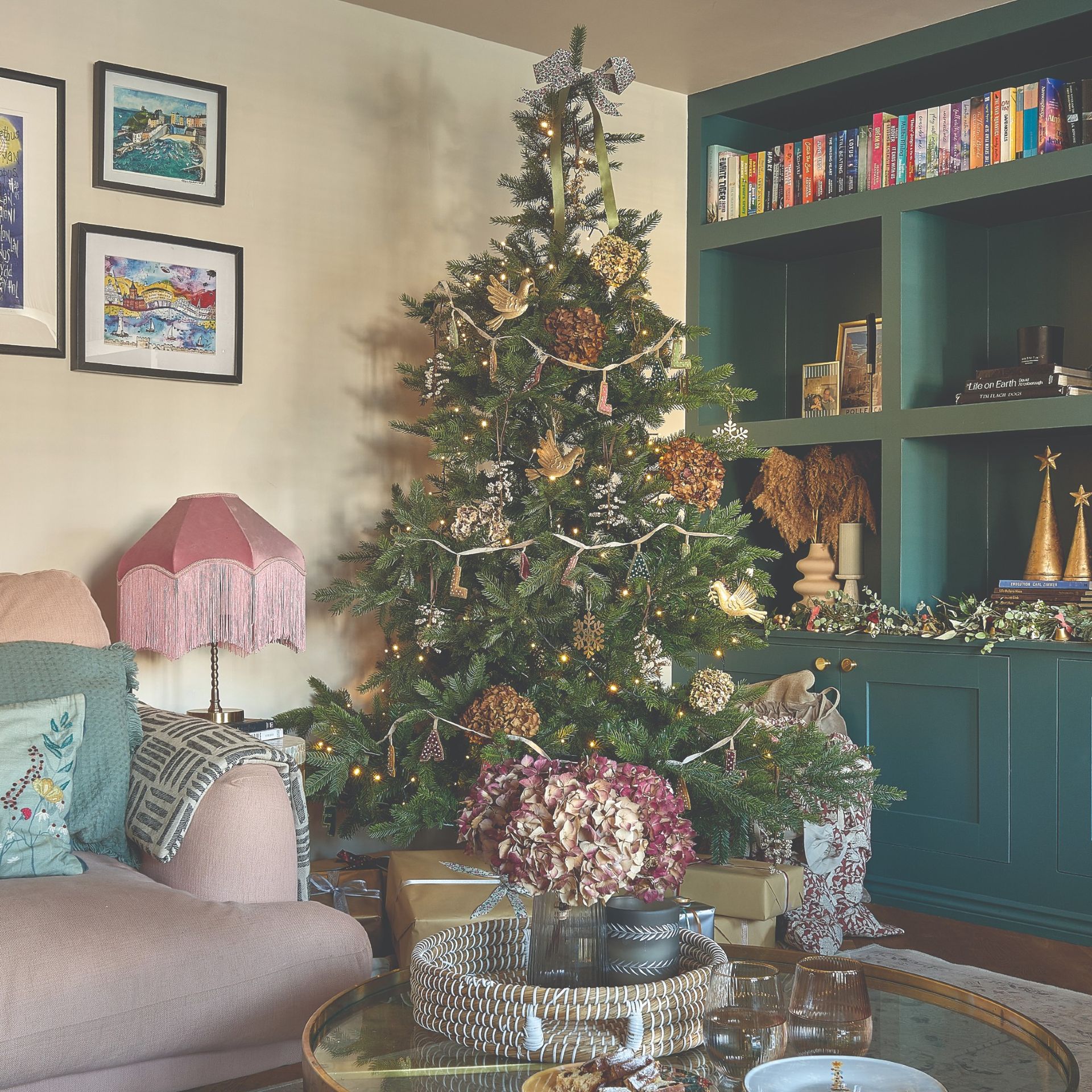 A living room with a built-in green bookcase decorated for Christmas with a traditional green tree adorned with hydrangeas and traditional decorations