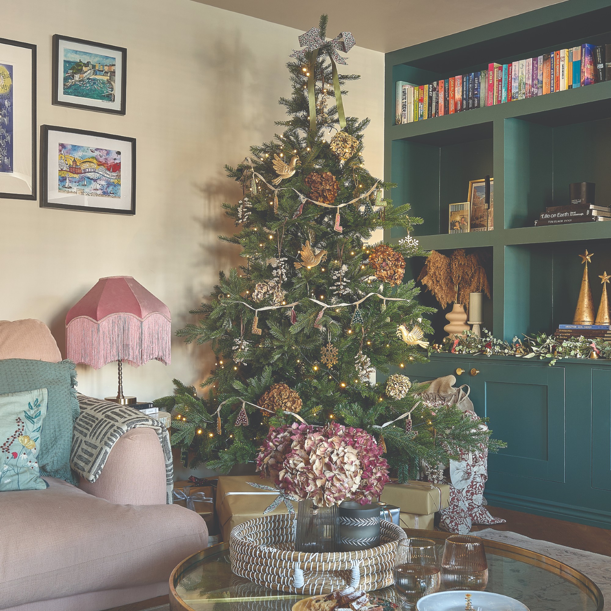 A living room with a built-in green bookcase decorated for Christmas with a traditional green tree adorned with hydrangeas and traditional decorations