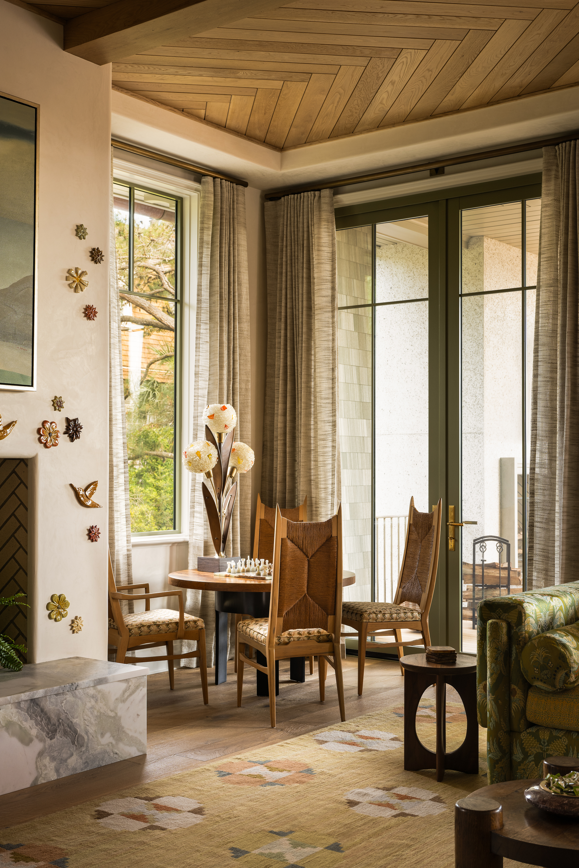 round table with four chairs around it in the corner of a living room with a chess board, timber ceiling, patterned rug, and fireplace mantel, with sheer curtains