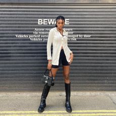 best chunky knee-high boots are shown in a street-style image of a woman wearing a white polo shirt with black shorts and black knee-high chunky boots and a black bag