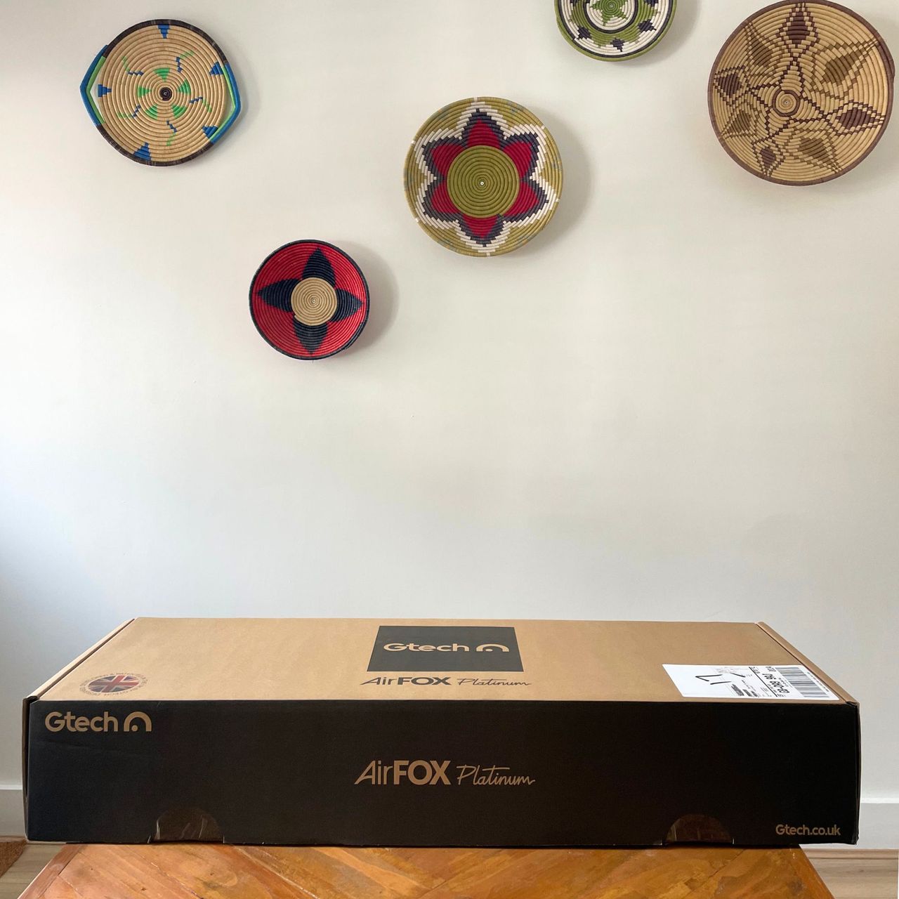 Gtech AirFOX Platinum Cordless Vacuum box sitting on a wooden table in front of a white painted wall