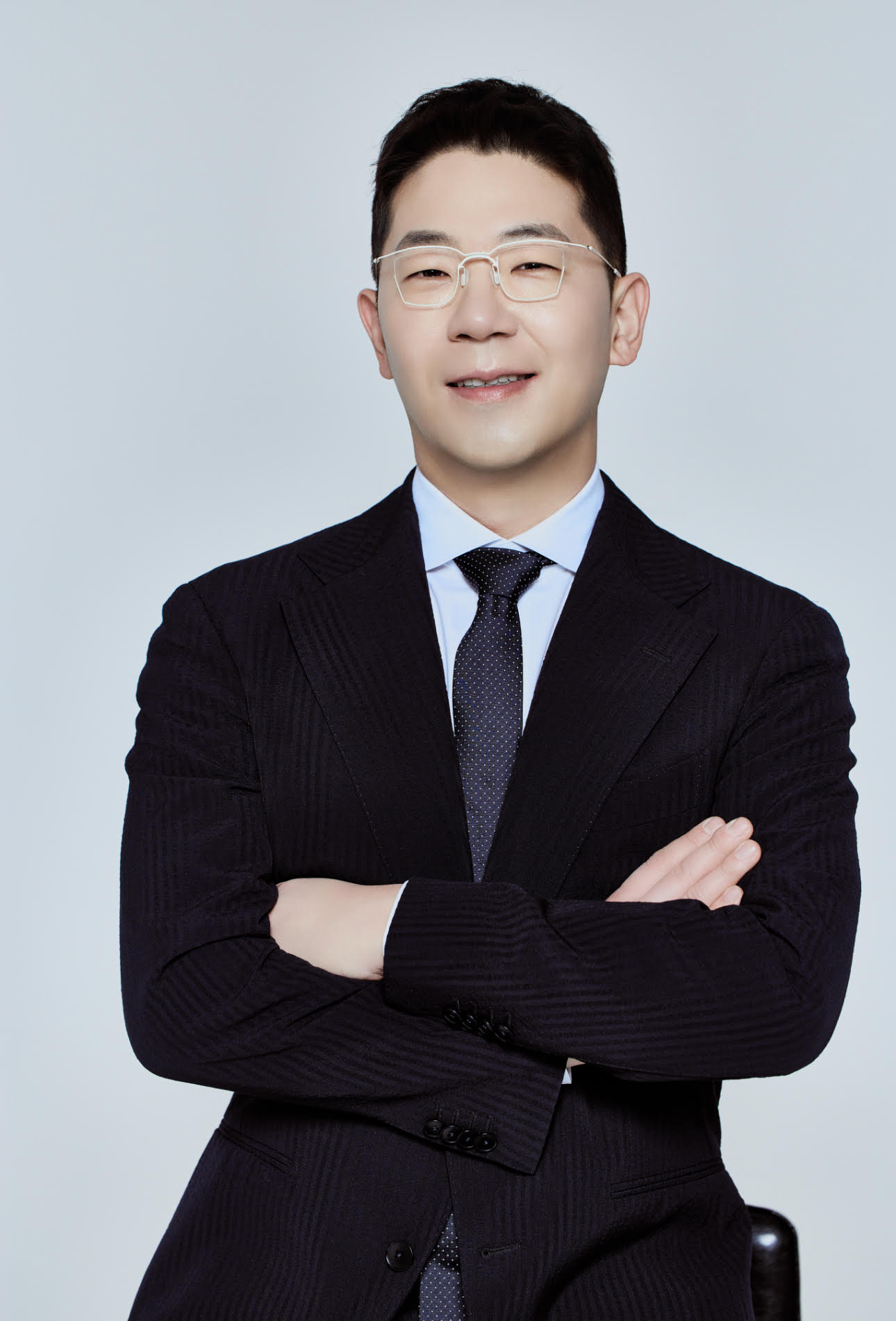 a korean man with glasses in a black suit and tie
