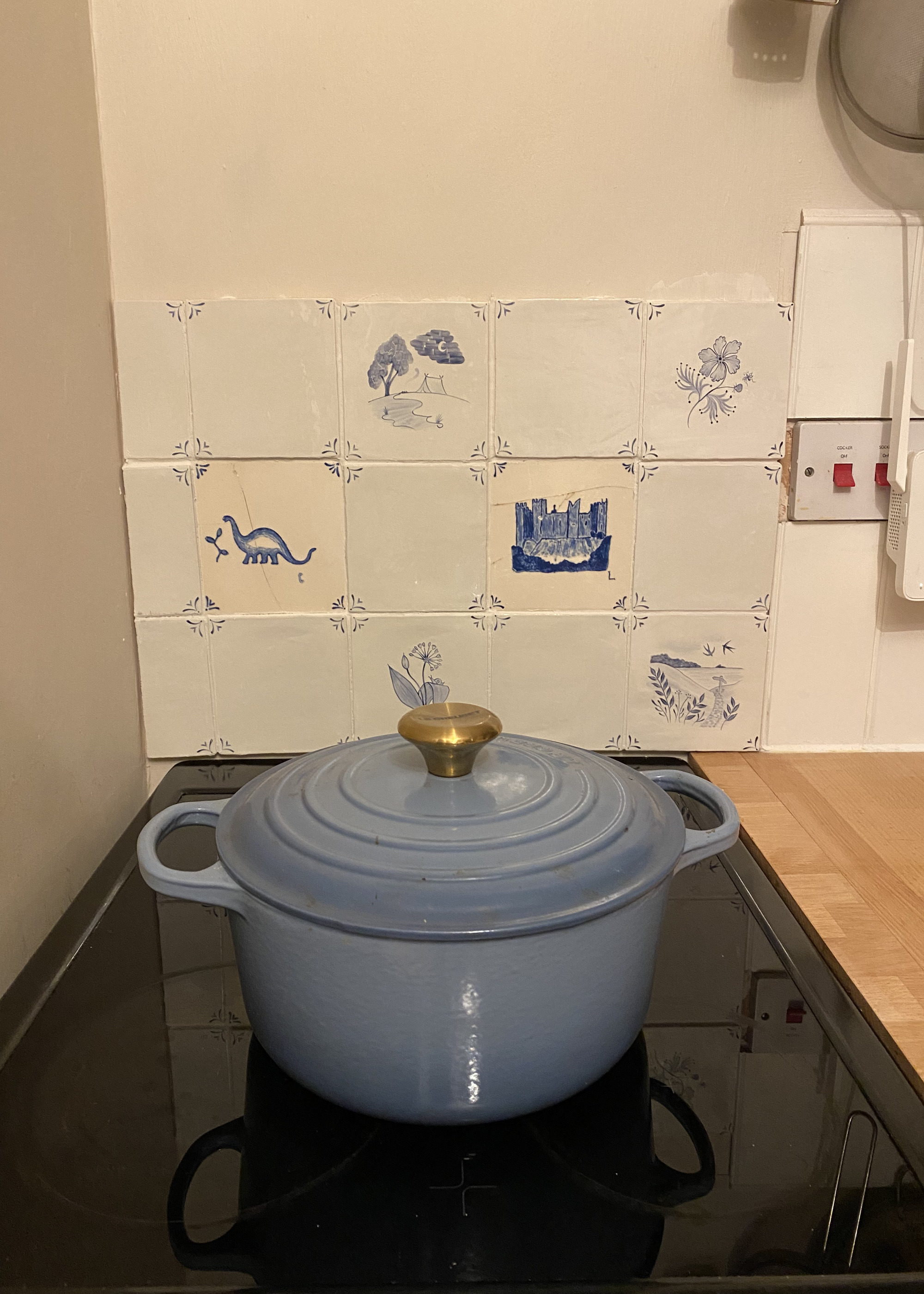 A stovetop with a blue Le Creuset dish and a Delft tiles backsplash in the background