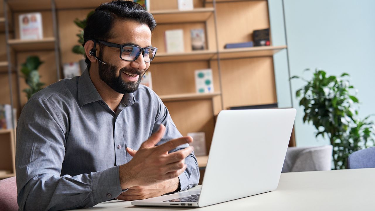 A financial adviser talks with a client on his laptop while in his office.