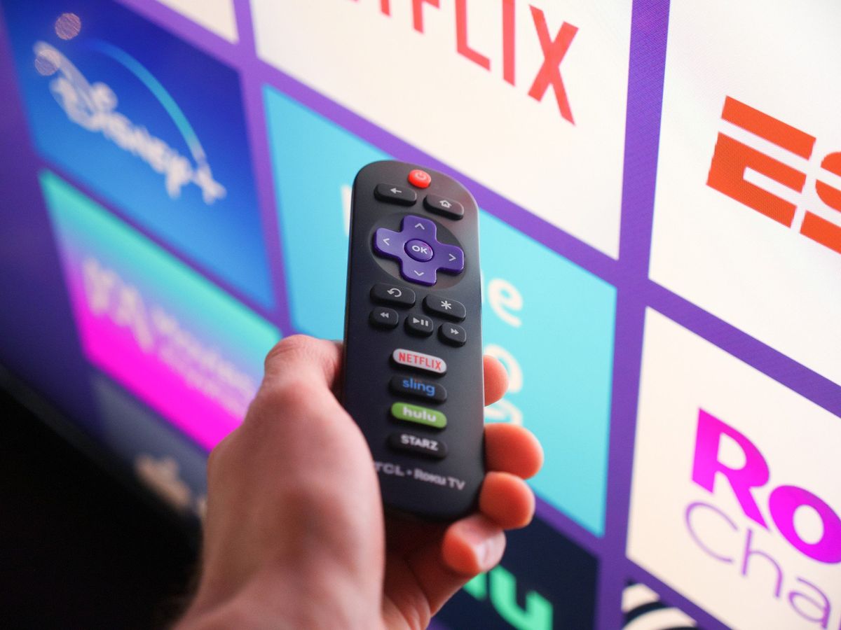 Roku remote in front of a TV running Roku OS