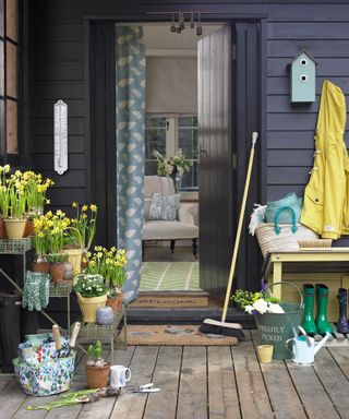 An example of how to decorate a front porch showing a porch area with dark paneling and plant pots holding flowers