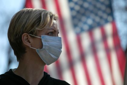 A woman wears a face mask in front of an American flag.