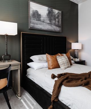 A dark bedroom with a gray accent wall, a black bed with white sheets, and a desk