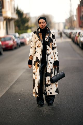 A woman at Milan Fashion Week's Fall 2025 Street Style in a cowprint fur coat, black east-west shoulderbag, black top, black pants