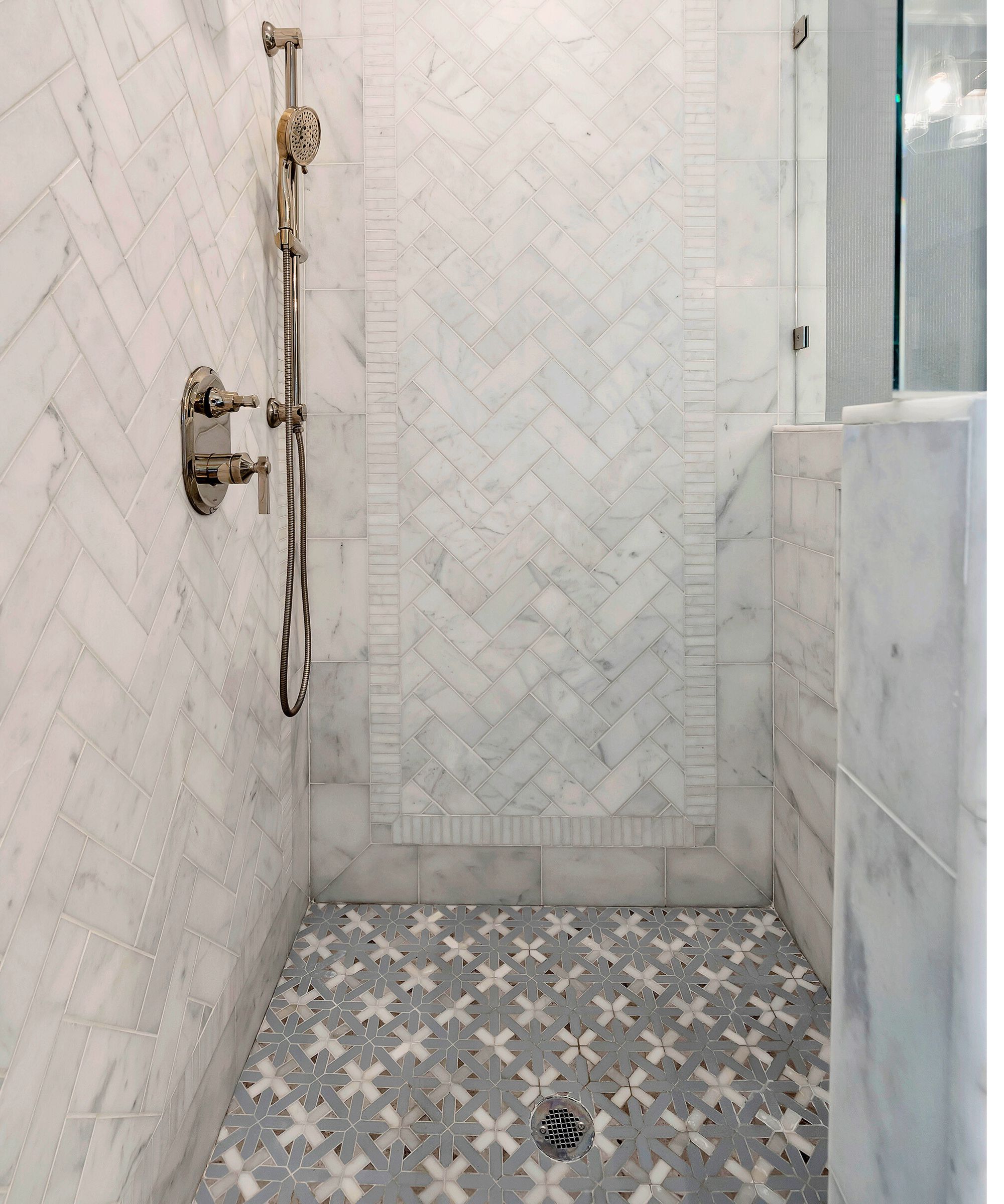 A tiled shower with brass hardware and marble half wall with glass screen