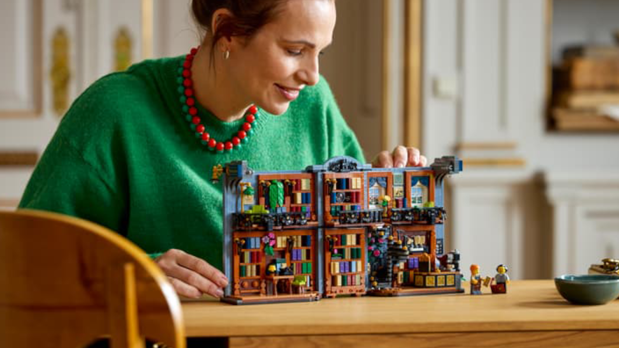 A woman displaying the Lego Bookstore: Book Nook on a table