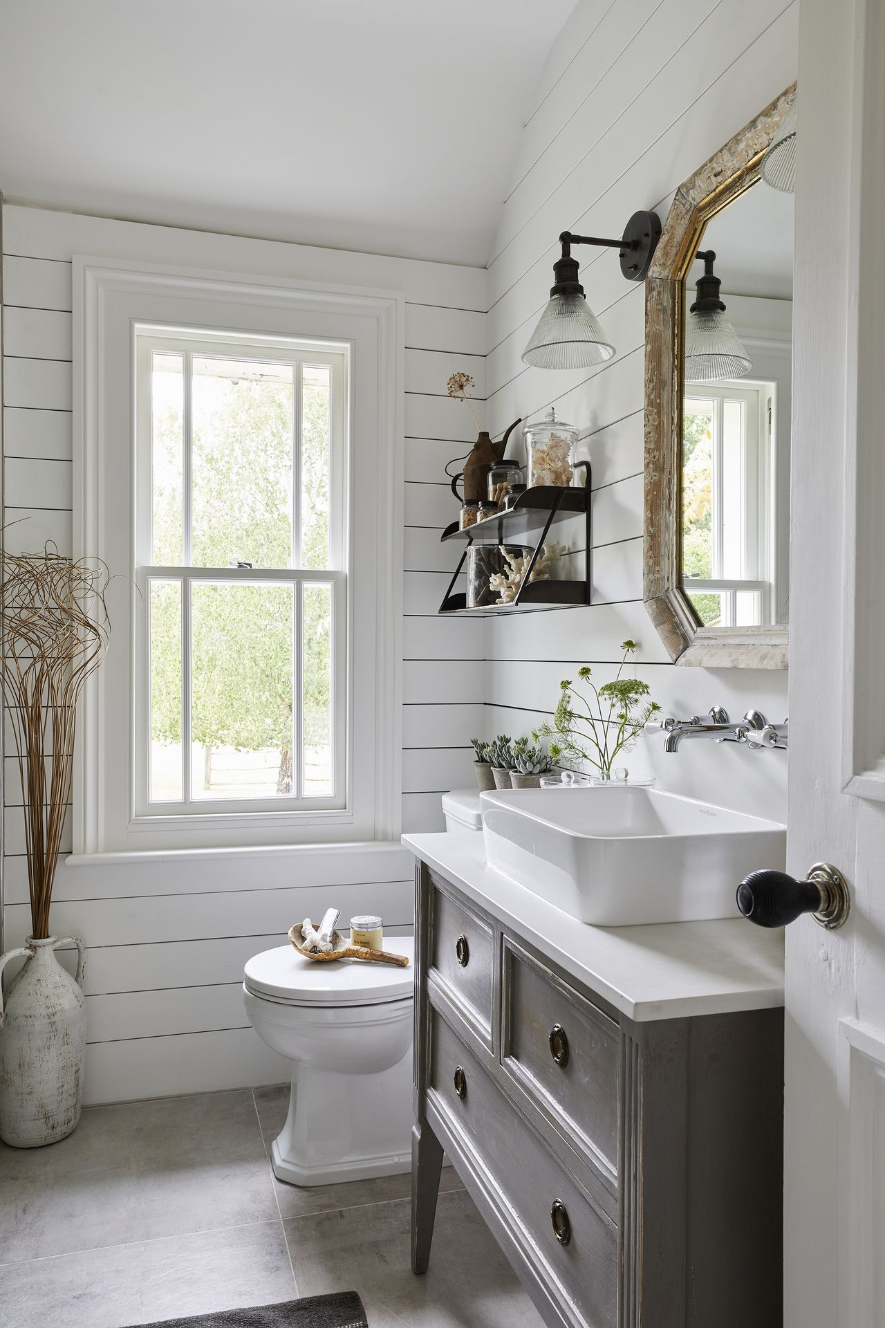 White bathroom with wooden walls, nightstand, black wall-hung shelf, antique mirror