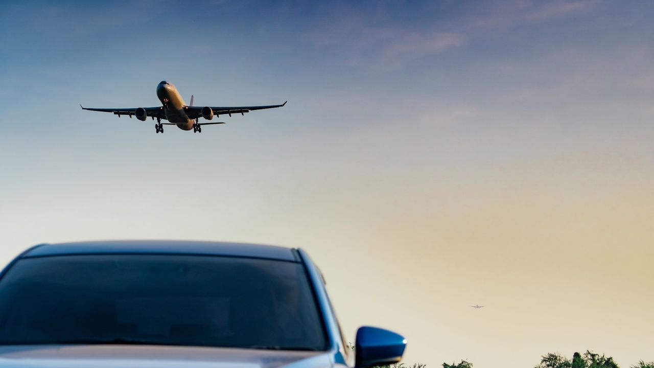 Plane flying in the sky above a car driving down on a road