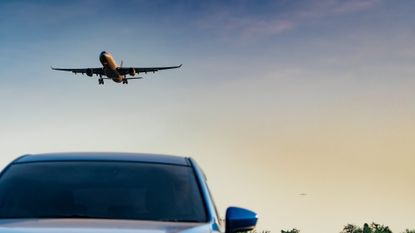 Plane flying in the sky above a car driving down on a road