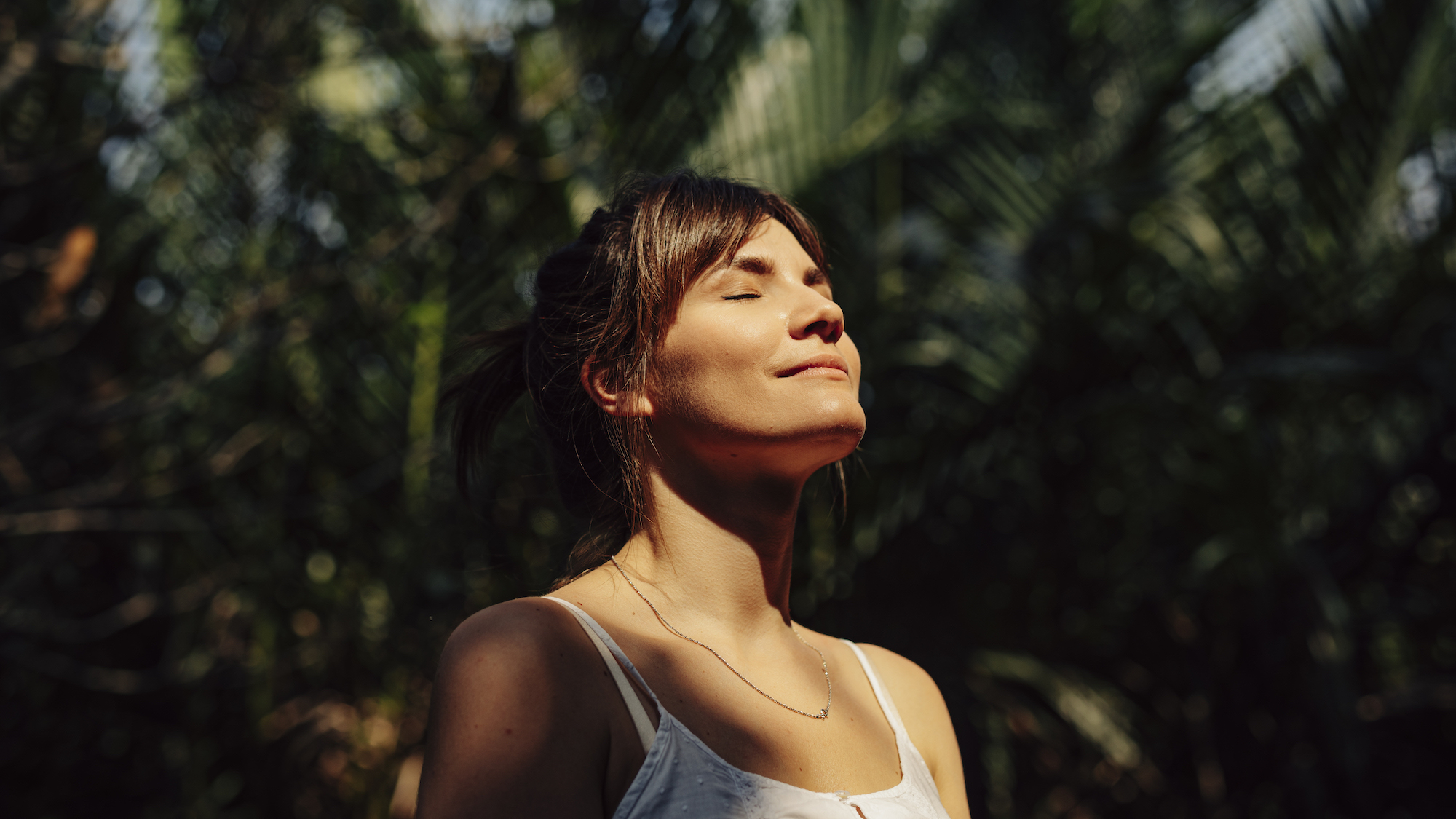 Woman with face in the sunshine surrounded by tropical banana leaves