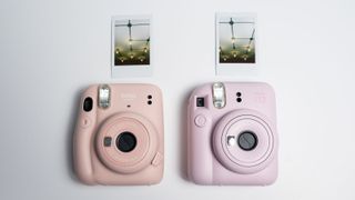Fujifilm Instax Mini 12 alongside Instax Mini 11 with instant prints from each camera on white background