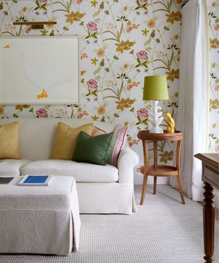 living room with floral pink and yellow wallpaper, a neutral couch with yellow and green throw pillows and vintage side tables with a large goose wall art