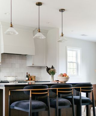 a white kitchen with three vintage inspired pendant lights above the island