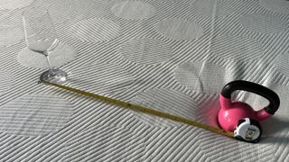 Image shows a tape measure and pink kettlebell placed on the Casper Snow hybrid mattress during the motion isolation test part of the review