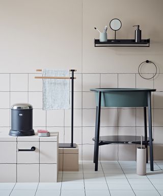 A bathroom with pale pink wall paint and tiles, and a green freestanding basin with a black shelf above it