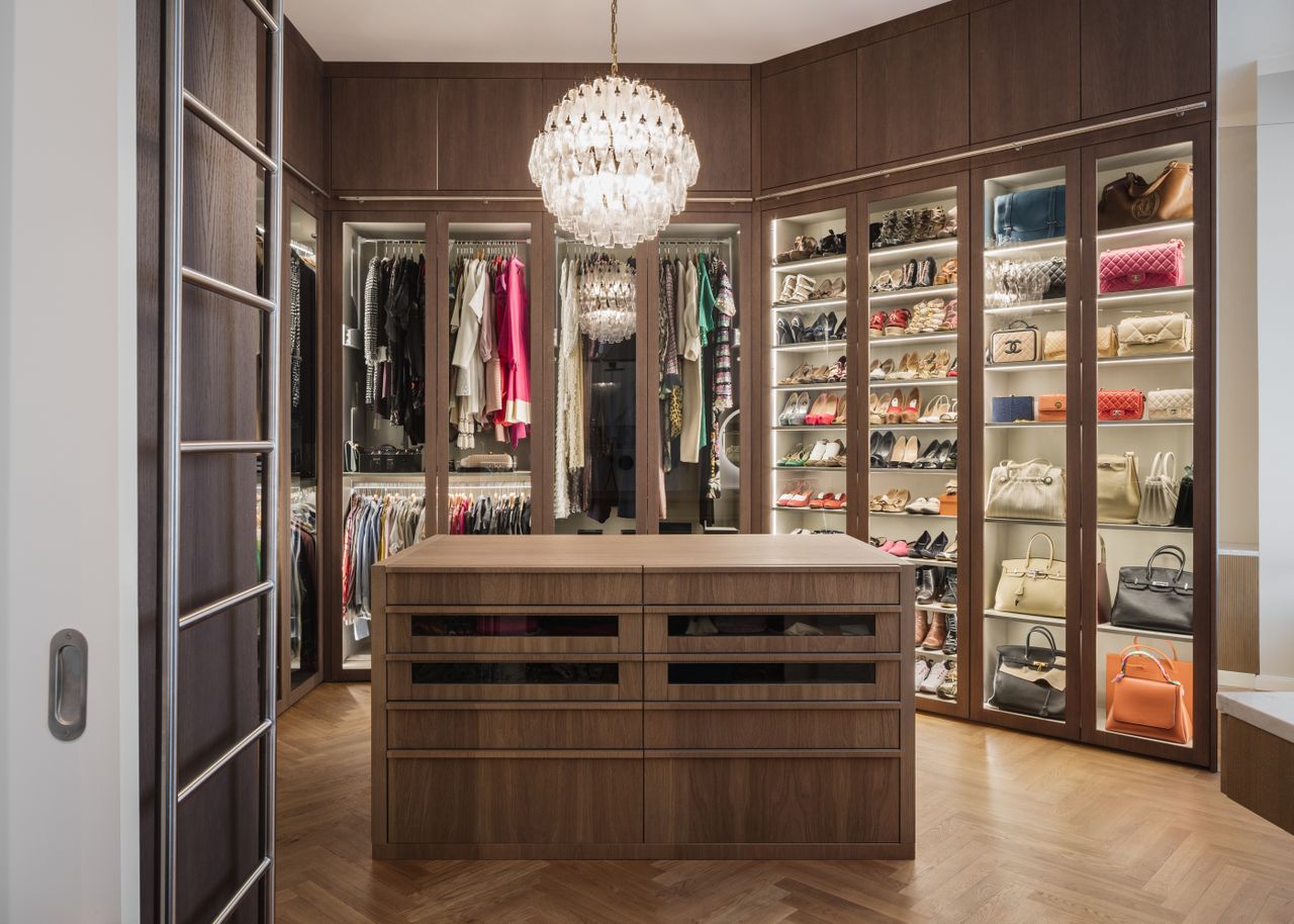 a wooden closet with a bag cabinet and clothes rails, illuminated by a chandelier