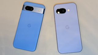 The Bay Google Pixel 8a (left) and Iris Google Pixel 9a (right) next to one another on a white desk surface.