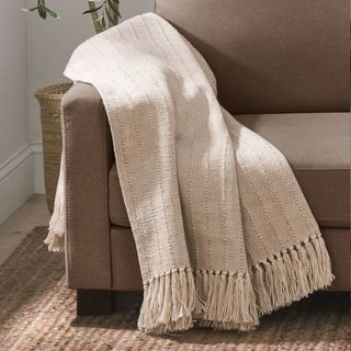 A brown leather couch with a beige throw blanket draped over the arm