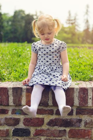 young girl sat on a wall with her shoes off