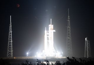 a very white, blurry view of a rocket in a timelapse photo to emphasize the blood moon high overhead