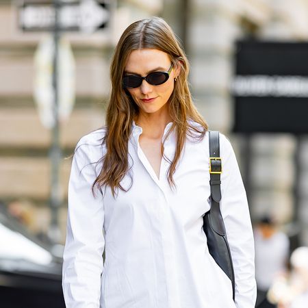 Karlie Kloss wearing a cinched button-down, a black skirt, a black bag, and black open-toe sandals 