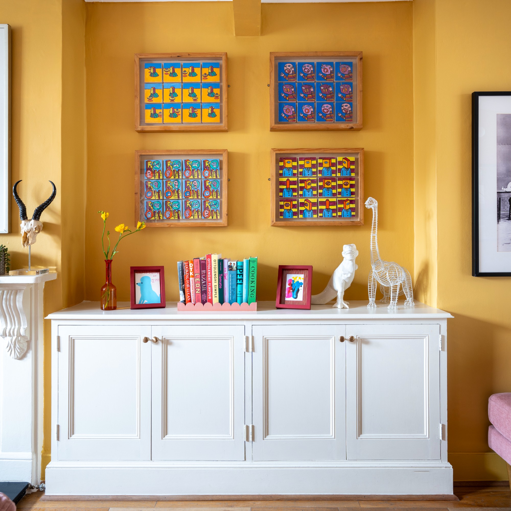 A bright yellow-painted living room with a gallery wall above a white sideboard displaying decorative items