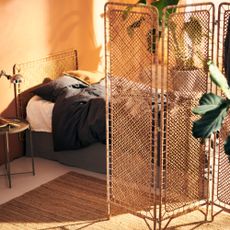 a beige, light-filled bedroom with bed, rattan room divider and rattan headboard