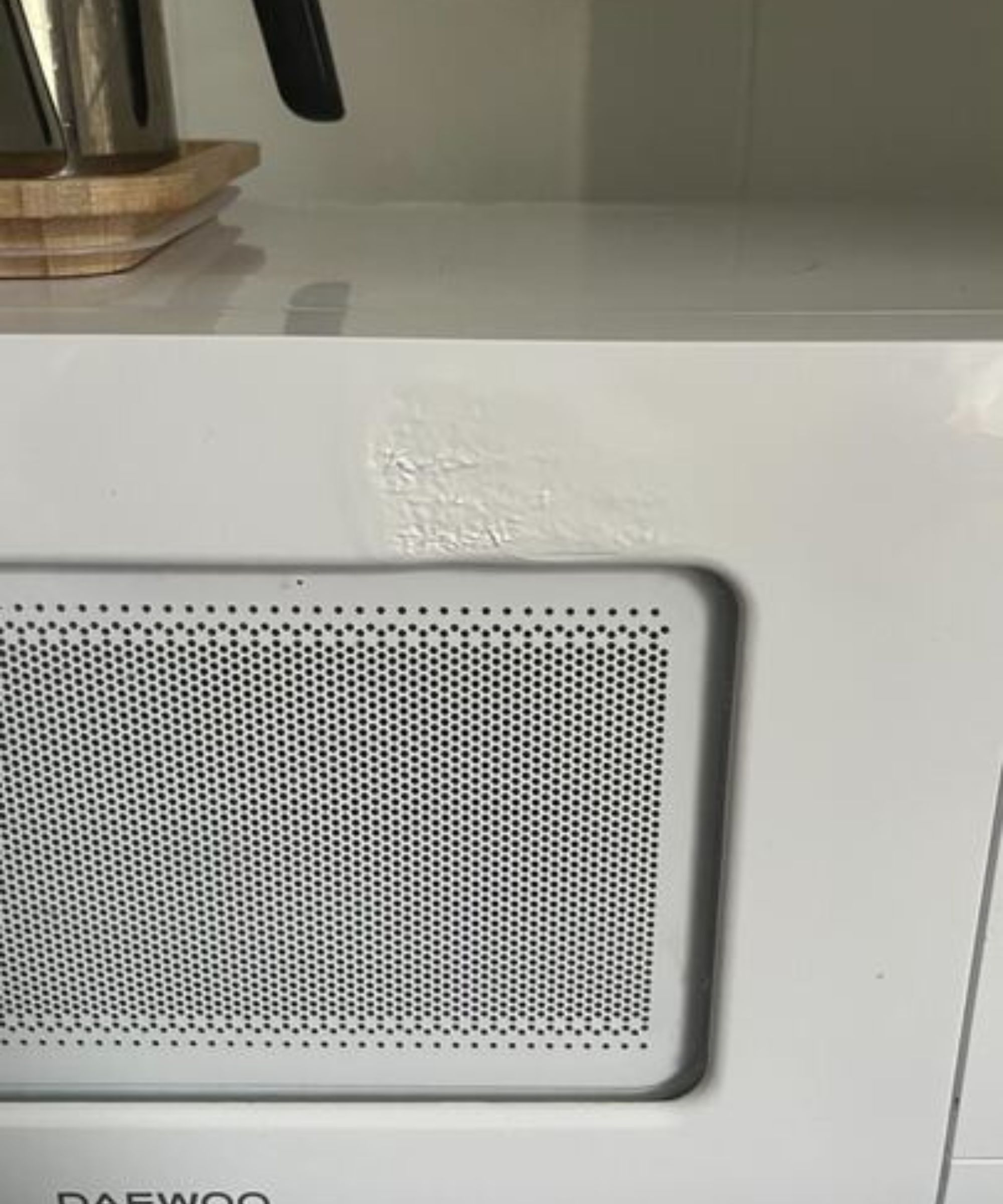 The front of a white plastic microwave with a melted spot.