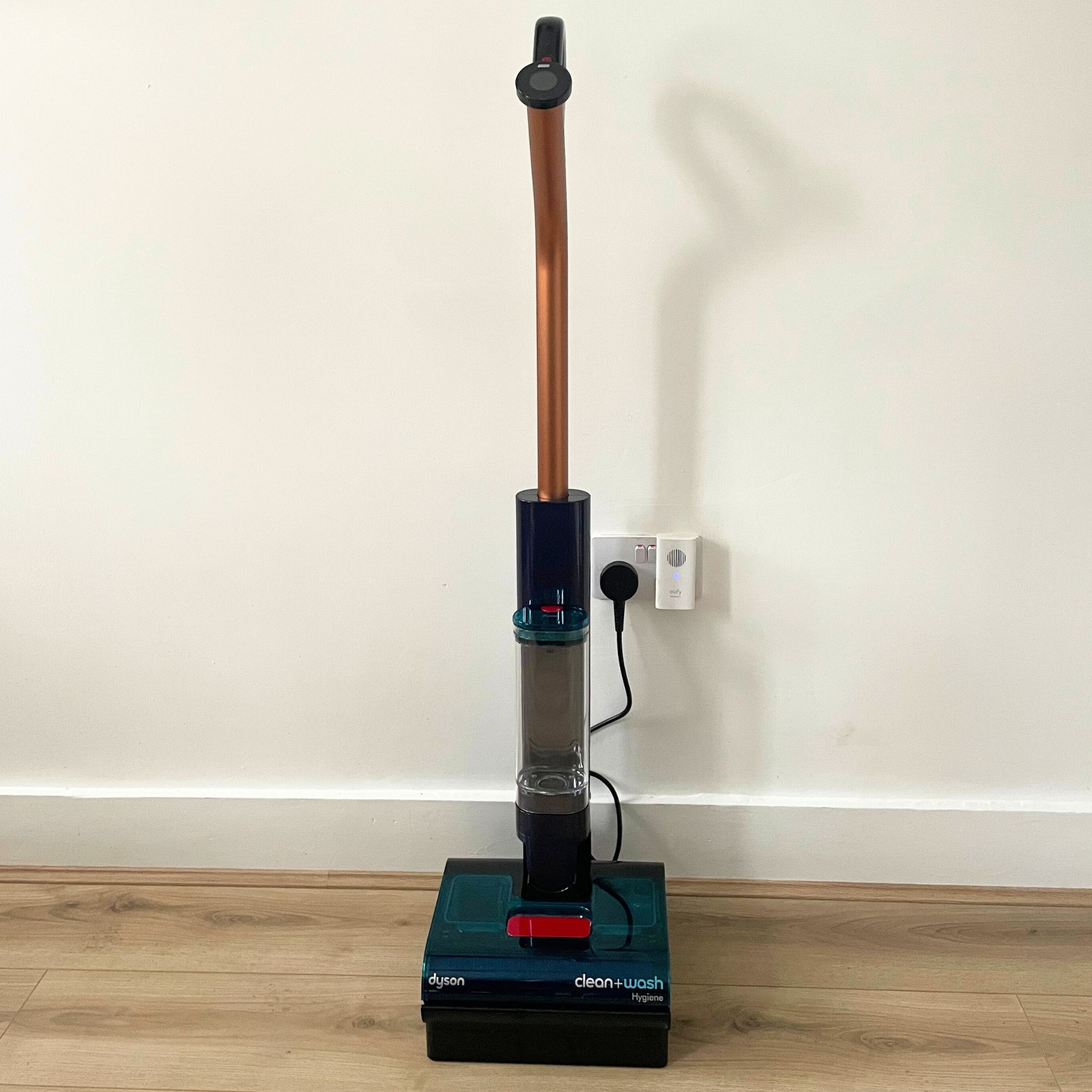 Dyson Clean+Wash Hygiene on its dock, sitting on wood-effect flooring in front of a white wall
