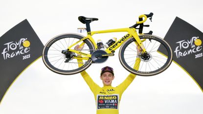 Jonas vingegaard on the podium at the tour de france 2023 holding his winning bike inthe air