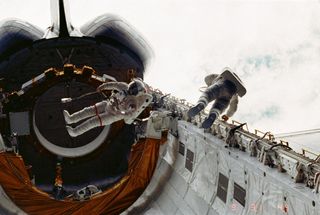 Astronauts Story Musgrave, left, and Donald Peterson float about in the cargo bay of the Earth-orbiting space shuttle Challenger during their April 7, 1983. It was the first spacewalk from a space shuttle.
