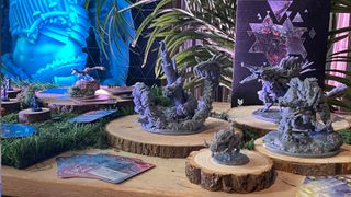 Miniatures from Horizon Forbidden West: Seeds of Rebellion on wooden circles across a table, with vegetation in the background