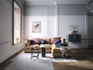 living room with white and grey walls, brown couch, coloured cushions, rug, artwork