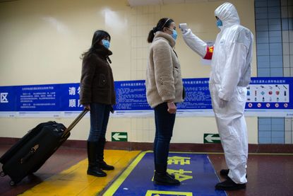 A woman wearing a mask gets her temperature checked.