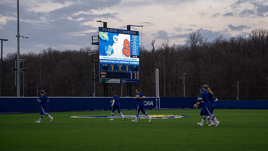 The University of Delaware softball players in blue uniforms walk towards center field. 