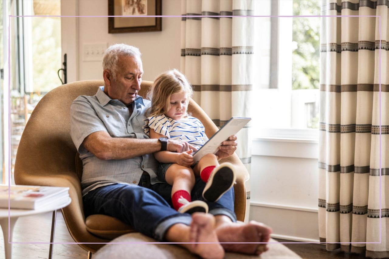 A grandfather with his granddaughter sat on his lap and reading a book