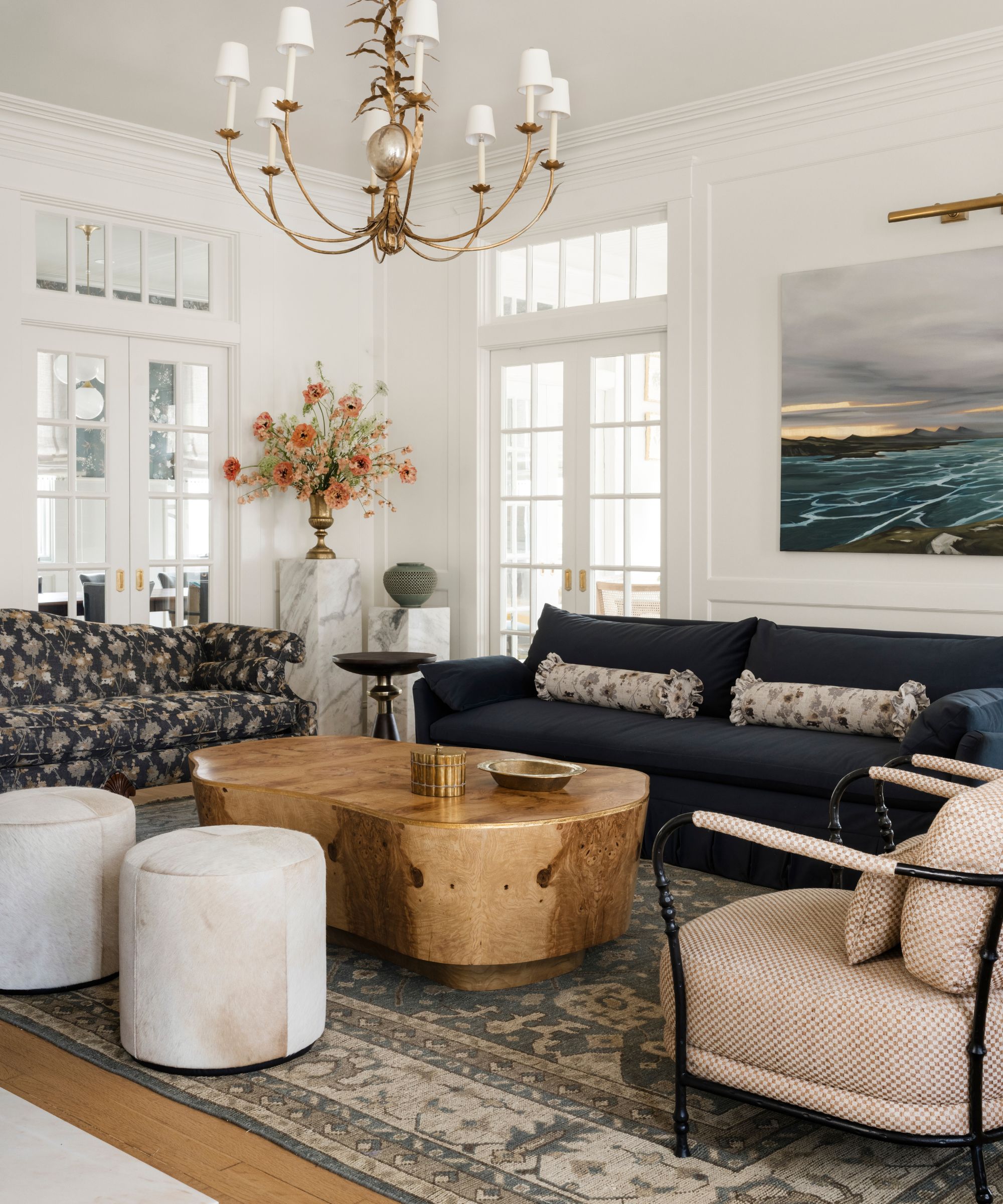 a white painted formal living room with large rug, navy sofa, floral vintage settee, wooden coffee table and iron armchairs