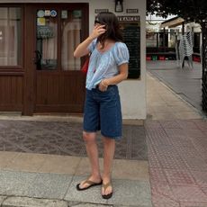 Woman wears blue blouse, denim jorts and suede sandals